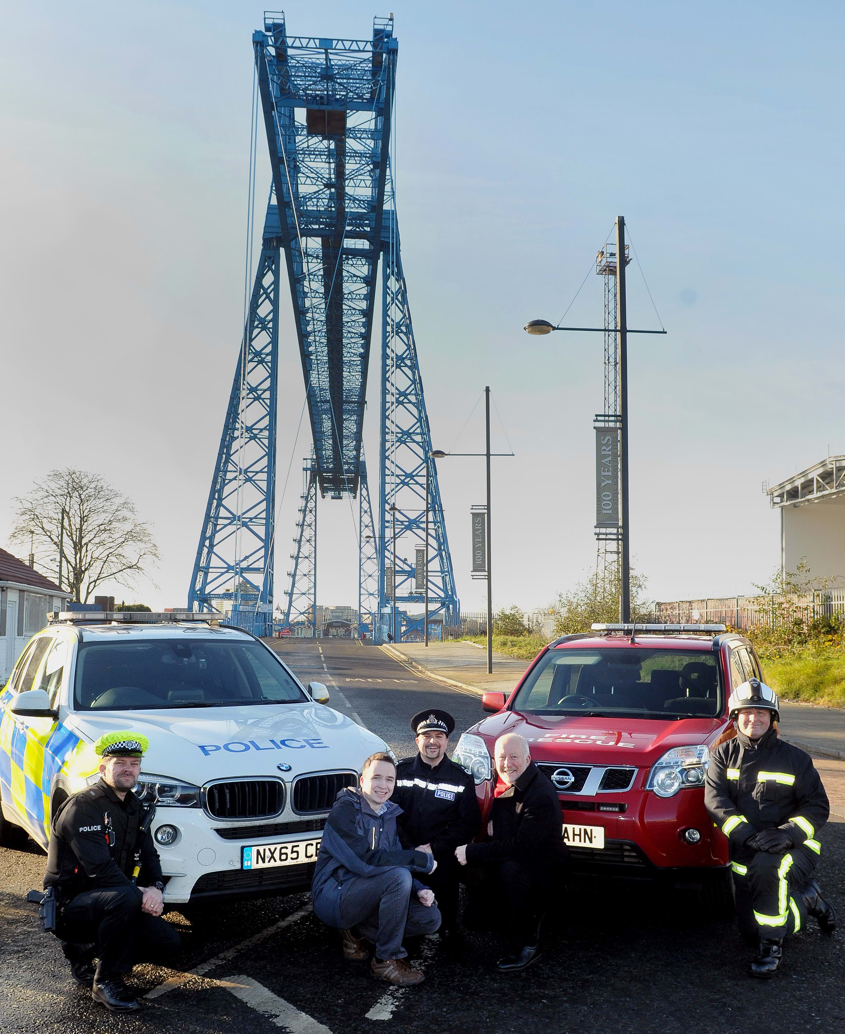 An image of David Robinson, Emergency Services and Andy McDonald MP crouched in front of emergency vehicles